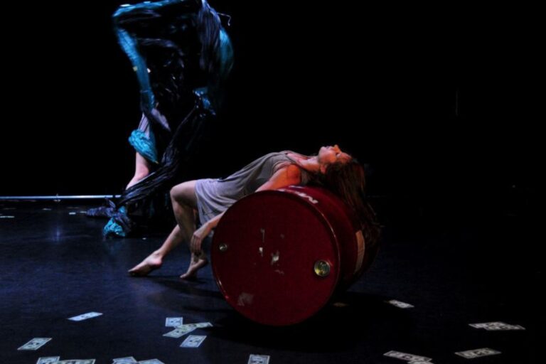 Photo de d'une danseuse allonger sur un brail tandis qu'une sorte de sac poubelle semble sur le point de lui sauter dessus, prise lors d'une représentation de Barils... et quoi d'autres ? Une création origianel de la Cie Mouvementé Danse.